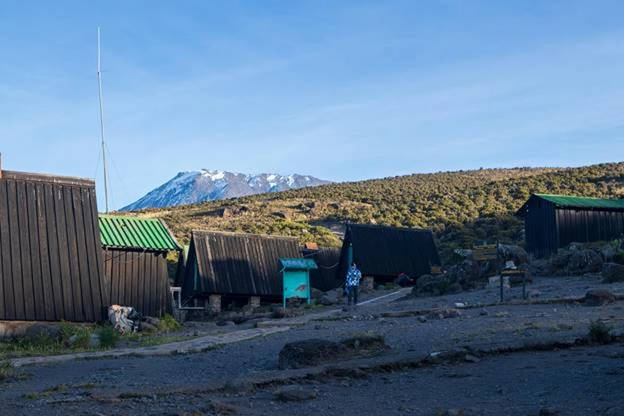 Accommodation huts on Marangu Mount Kilimanjaro trekking route. Snowcapped summit on a sunny day.