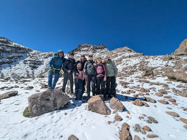 Mountain climber victory posing on Mount Kenya trek with peaks and campsite up ahead. Blue sunny sky