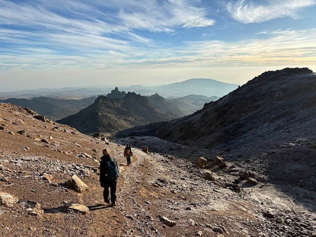 Two mountain climbers trekking Mount Kenya’s alpine snowcapped desert on a sunny day.