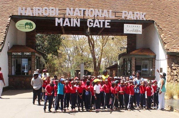 A group of primary school students school trip standing in front of Nairobi National Park main gate