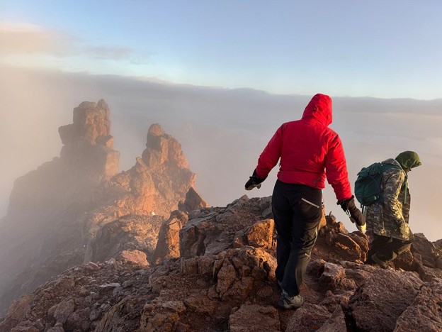 A hiker and guide walking through a rocky ridge wearing jackets, gloves, and cargo pants for warmth.