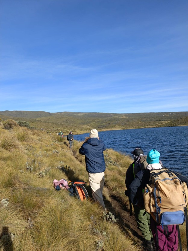 hikers and porters carrying large backpacks along the shores of Lake Ellis on  Mount Kenya trail 