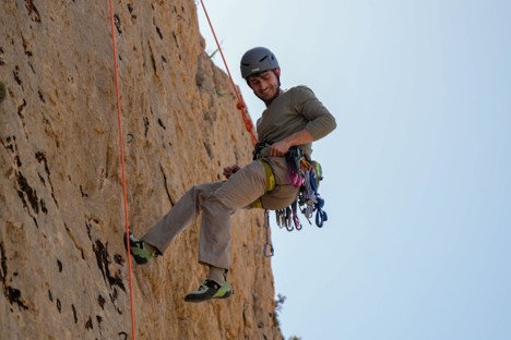 A technical climber wearing layered alpine clothing on a steep mountain rock face