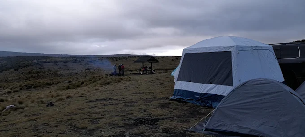A spacious mess tent and sleeping tent at a Mount Kenya campsite. Hikers in a gazebo, campfire