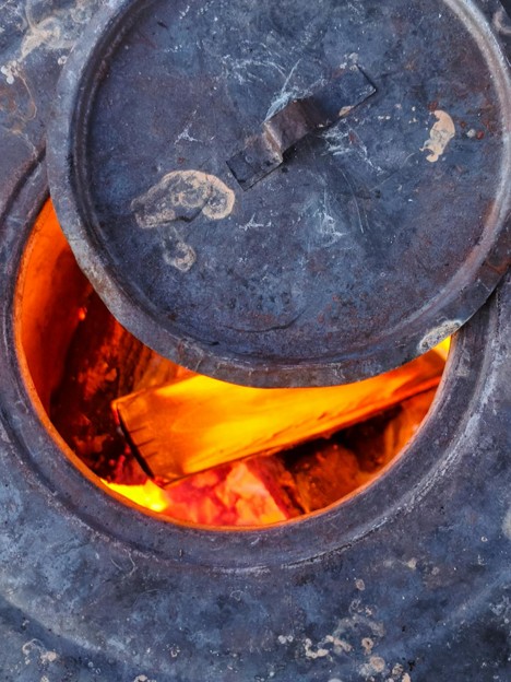 A burning warming stove partly covered with a metal lid. Red hot wood inside a