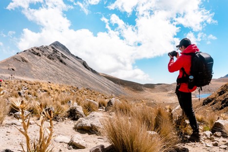 A hiker photographing the mountain landscape with a camera on a sunny day