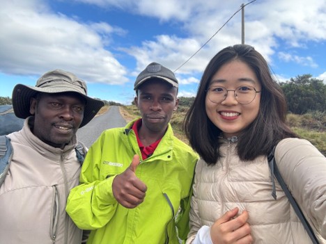 A Mount Kenya hiker taking a photo with a guide and porter on the side of the road