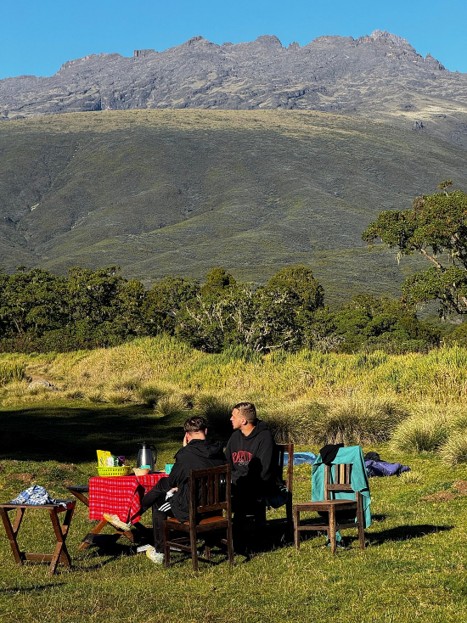 Two hikers sitting on a dining set enjoying breakfast on a sunny morning before the hike starts