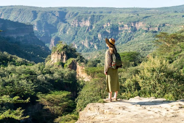 A lady on safari standing on a cliff looking at the gorges and valleys of Hell’s Gate National Park