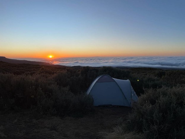 A white camp set up on the slopes of Mount Kenya at sunset, cloud line seen below