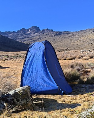 A blue portable tent toilet on Mount Kenya on a clear sunny day, main peaks in the distance ahead